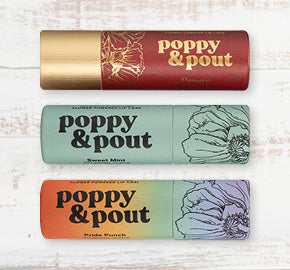 Three lip balm tubes from Poppy & Pout on a wooden surface